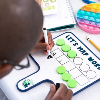 student writing on dry erase word-mapping board